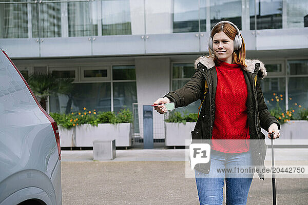 Smiling woman wearing wireless headphones and unlocking car with remote control key