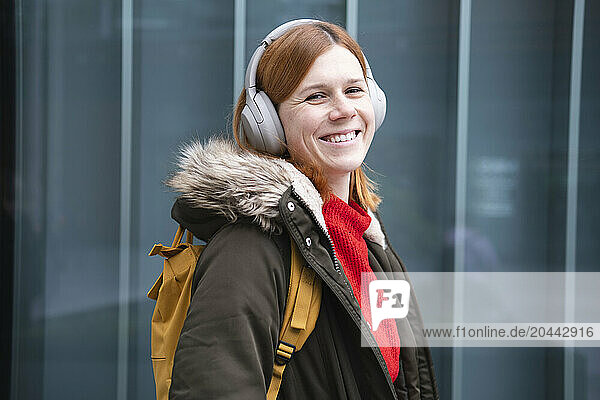 Happy redhead woman listening to music through wireless headphones