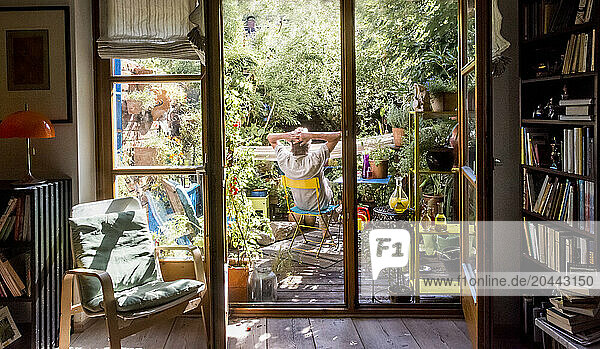Senior man with hands behind head sitting on chair in garden