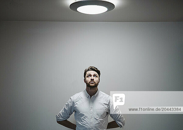 Businessman standing under electric light in front of wall