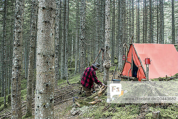 Senior man preparing bonfire near tent in forest