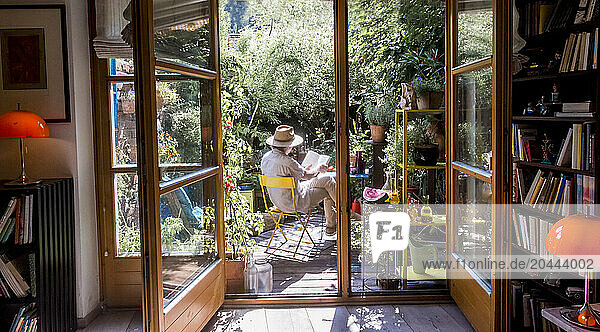 Man wearing hat and reading book on chair in garden