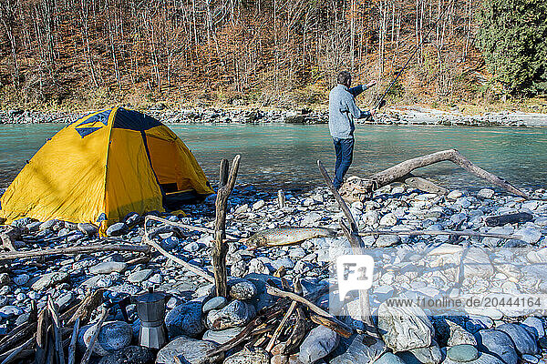 Senior man fishing with rod in river near tent on sunny day