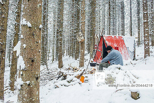 Senior man enjoying bonfire in snow near tent at forest