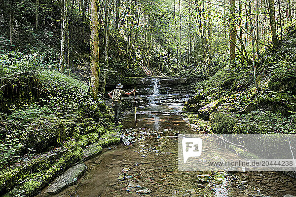Senior man standing near water stream in forest