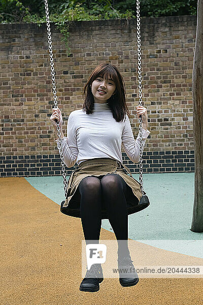 Young woman sitting on swing at public park