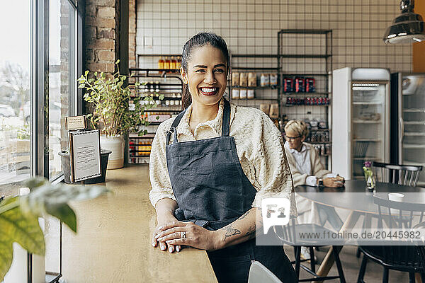 Portrait of happy female owner with tattooed arm standing near table in cafe