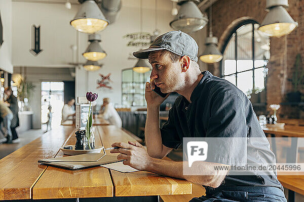 Male owner talking on smart phone while sitting in coffee shop
