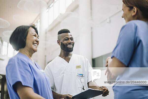 Smiling male medical professionals discussing with female colleagues in hospital