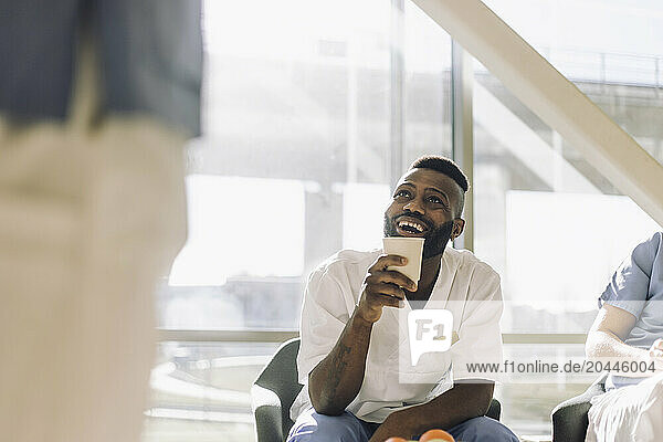 Happy male medical worker holding disposable cup while sitting in cafeteria