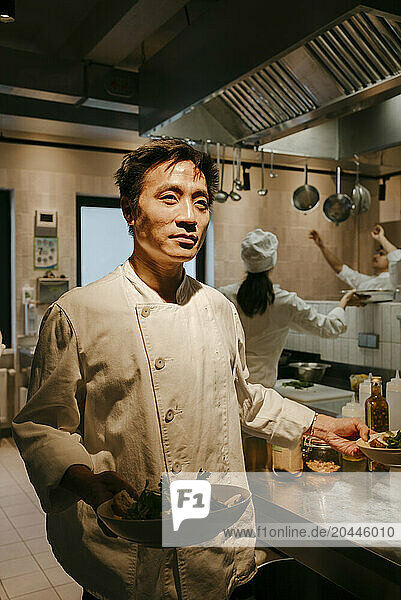 Male chef standing with salad bowl at illuminated commercial kitchen