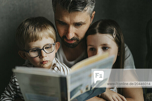 Father reading book with son and daughter at home