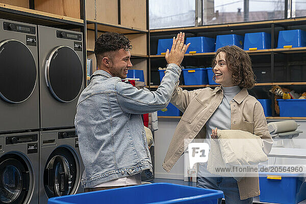 Happy young couple giving high-five at laundromat