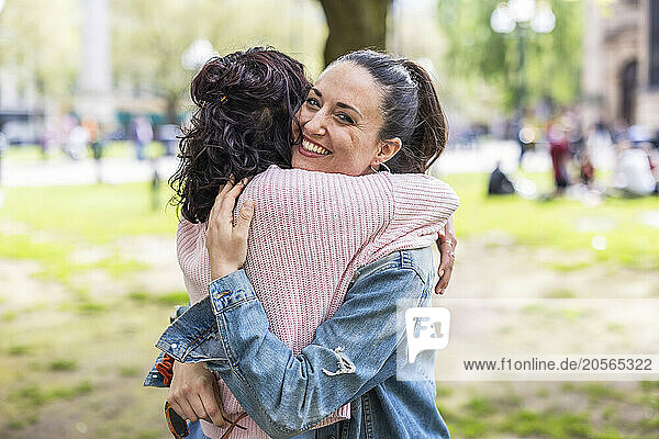 Smiling woman hugging female friend standing at park