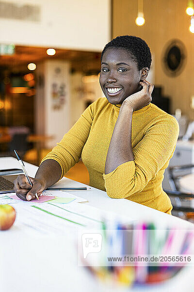 Smiling businesswoman writing on adhesive note at office