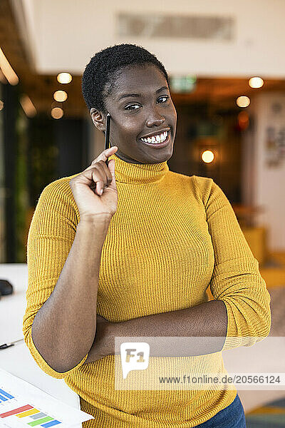 Happy businesswoman holding pencil and standing near desk at office