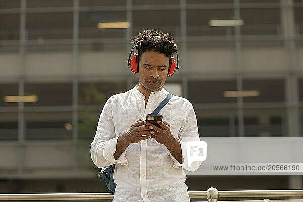 Man using smart phone and wearing wireless headphones at bus stop