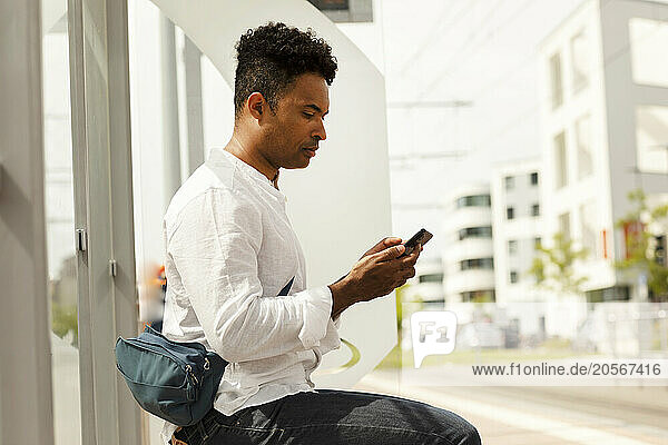Man with fanny pack using smart phone and sitting at bus stop