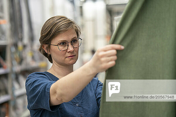 Mature woman in eyeglasses examining cloth in supermarket