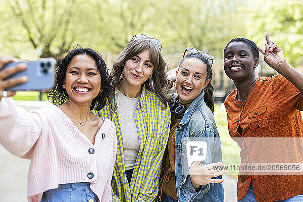 Smiling woman taking selfie with multiracial friends through smart phone