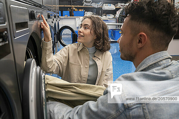 Young customers removing sheet from washing machine in laundromat
