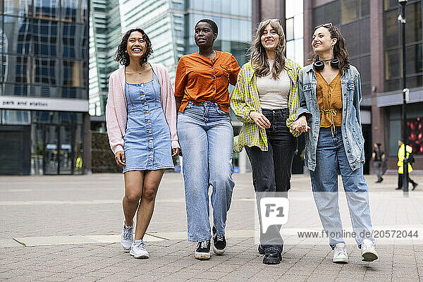 Smiling female friends walking on footpath in city