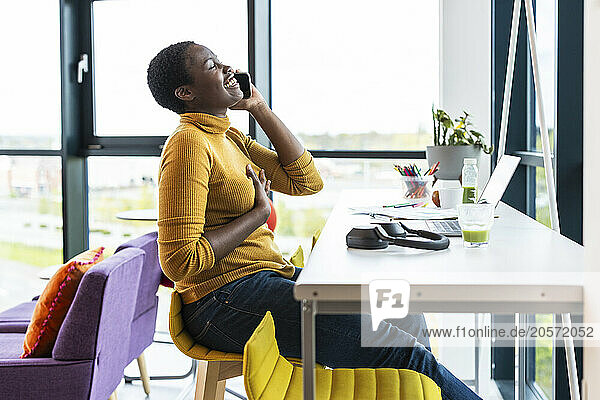 Happy businesswoman talking on smart phone sitting at desk in office