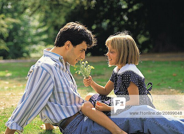 Father & child girl sitting outdoors in the park.