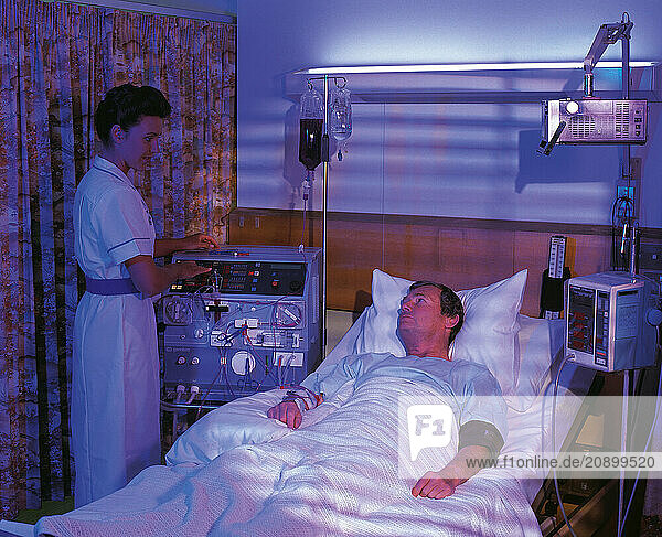 Medical hospital. Nurse with male patient in bed undergoing renal dialysis treatment.