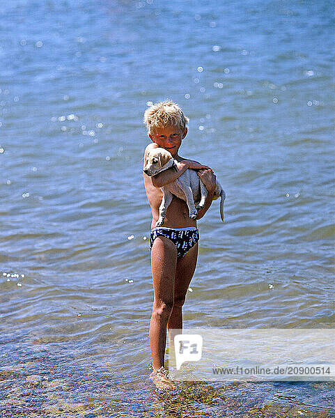 Australia. Sydney. Manly Dam. Boy with his puppy dog standing in shallow water.