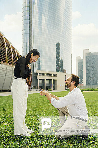Happy man proposing woman in front of buildings