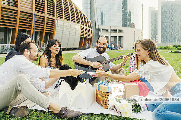 Happy man playing guitar with friends enjoying picnic in park