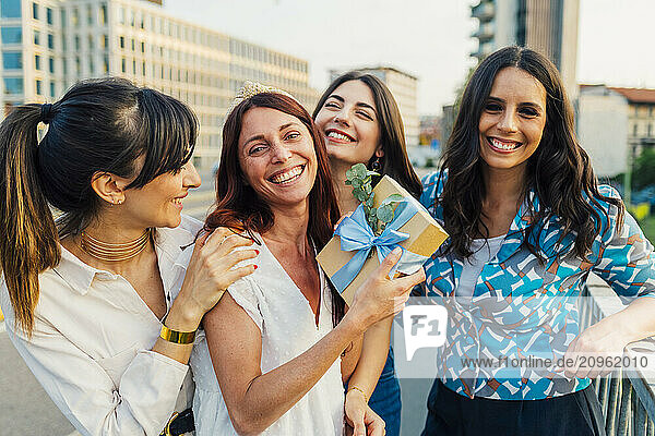 Cheerful woman holding gift box with friends in front of buildings