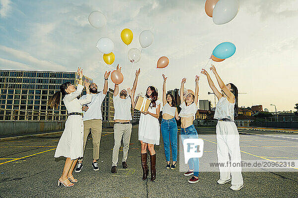 Cheerful friends celebrating woman's birthday with balloons on road