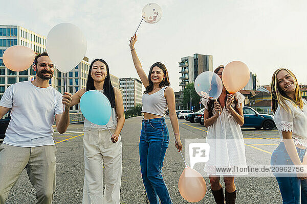 Happy friends holding balloons on road under sky