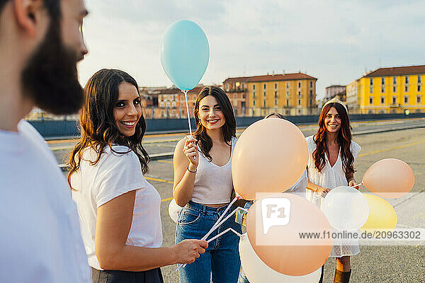 Happy friends standing with balloons and having fun on road