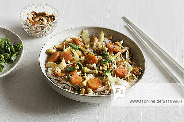 Bowl with fried white cabbage  carrots  spring onions and roasted cashew on rice noodles