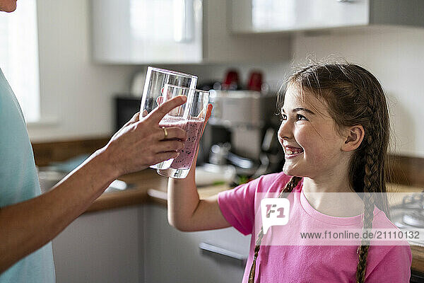 Happy girl toasting milkshake glass with mother at home