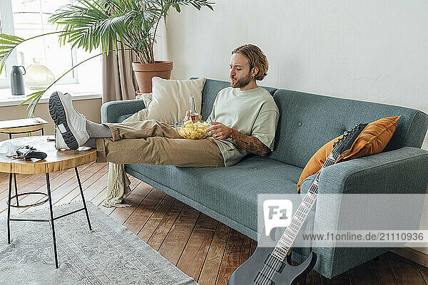 Man with snacks and beer bottle sitting at home