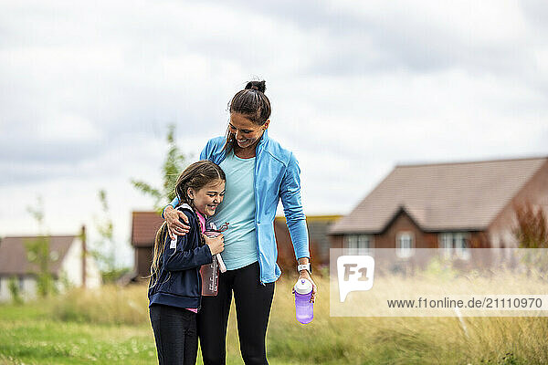 Woman holding water bottle and embracing daughter