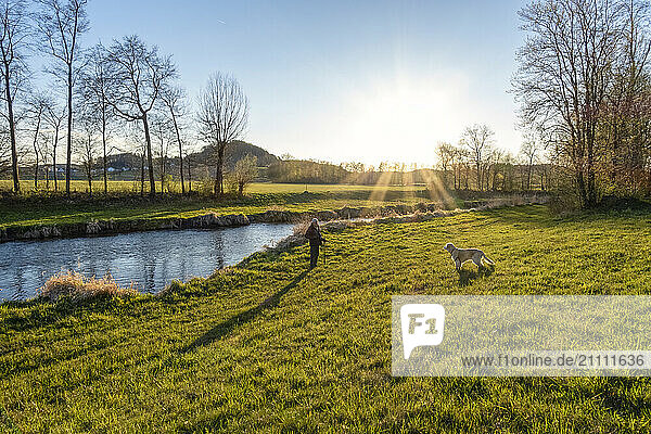 Man with dog standing near river at sunset