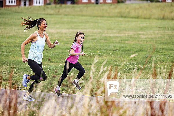 Happy mother and daughter spending leisure time running on footpath