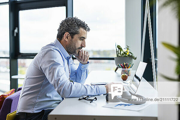 Thoughtful businessman working on laptop at co working space