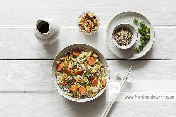 Bowl with fried white cabbage  carrots  spring onions and roasted cashew on rice noodles