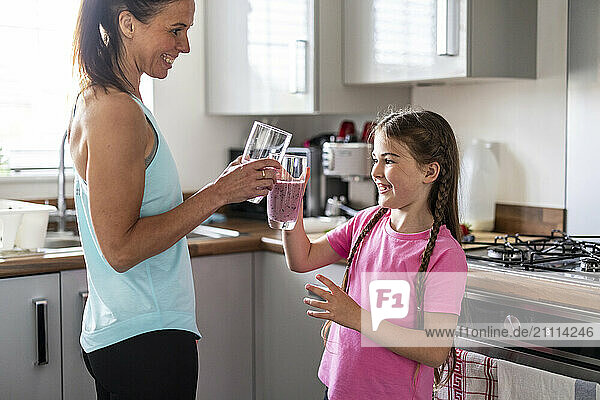 Mother and daughter toasting milkshake glasses in kitchen at home