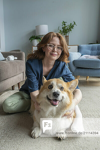 Smiling woman with Welsh Corgi dog sitting at home