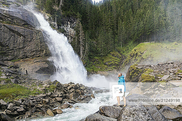 Man standing on rocks looking at Krimml Waterfalls in Austria's Hohe Tauern National Park  surrounded by mountains and nature.