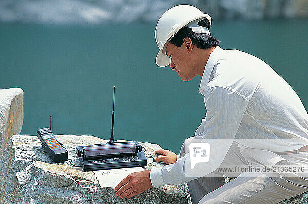 Singapore. Technology. Engineer outdoors using satellite phone with printer.