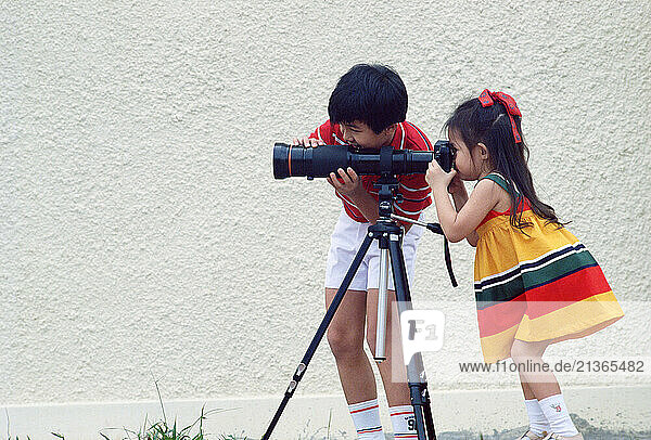 Singapore. Children. Little boy & girl looking through camera lens on tripod.