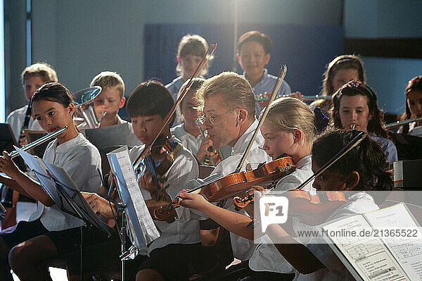 School teacher and children in orchestra music lesson.